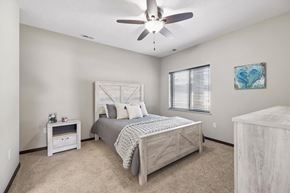 Lincoln townhouse for rent - Staged apartment bedroom with ceiling fan, carpet, wood-look bed frame, dresser, and window with blinds.