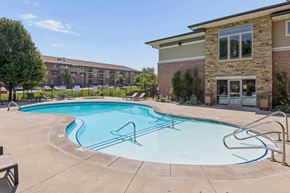 Omaha townhouse for rent - Outdoor swimming pool at Villas of Omaha at Butler Ridge with lounge chairs, entry steps, and the community clubhouse.
