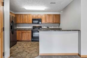 Omaha triplex for rent - Kitchen with wood cabinets, black appliances, speckled countertops, and a wide breakfast bar overlooking the living area.
