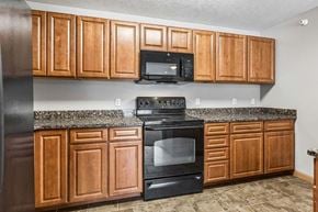 Omaha triplex for rent - Kitchen with warm wood cabinets, speckled countertops, a black oven and overhead microwave, and tile flooring.