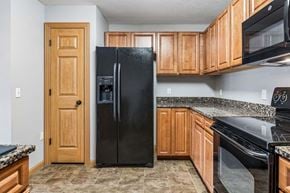 Omaha triplex for rent - Kitchen with warm wood cabinets, speckled countertops, black appliances, and tile flooring.