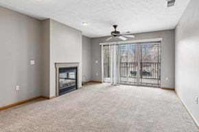 Omaha triplex for rent - Living room with soft carpeting, a fireplace, ceiling fan, and sliding glass doors opening to a balcony.