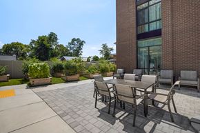 Frederick apartment for rent - a patio with a wooden table and chairs and a brick building in the background