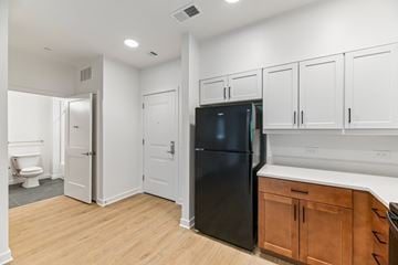 Rockville apartment for rent - A black refrigerator is in a kitchen with white cabinets and a wooden floor.