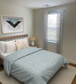 Odenton apartment for rent - A bed with a blue comforter with white dots is in the foreground of a room with a window and a picture on the wall.