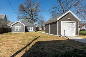 Evansville apartment for rent - Rear and side view of a one-story house with gray siding, white trim, detached garage, and grass yard with walkway between structures.