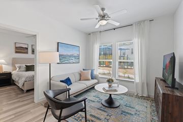 Converse apartment for rent - A living room with a white couch, a chair, a bed, a ceiling fan, and a painting on the wall.