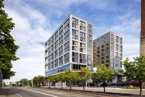 Cleveland apartment for rent - A modern multi-story building with a glass facade is situated on a street corner with trees and other buildings in the background.