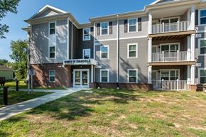 Evansville apartment for rent - Exterior view of multi-story apartment building with brick base, siding, balconies, and entrance labeled Homes of Evansville.