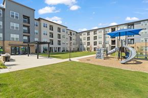 Fort Worth apartment for rent - A playground with a slide and a green lawn in front of apartment buildings.