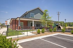 Charlotte apartment for rent - Community building exterior with a mix of brick and siding, showcasing a covered entry, walkway with ramp access, and adjacent playground equipment.