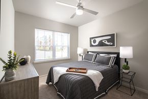 Charlotte apartment for rent - Bright bedroom interior with a central bed, decorative pillows, and a wall art piece above, accented by a window allowing natural daylight into the space.
