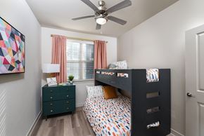 Austin apartment for rent - Bedroom featuring a large window, ceiling fan, wood-style flooring, and a functional layout with space for multiple sleeping arrangements.