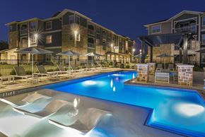 Mckinney apartment for rent - A swimming pool in front of apartment buildings at night.