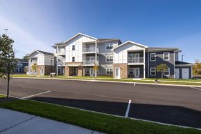 Saratoga Springs apartment for rent - Exterior view of an apartment community with a mix of siding and stone finishes, organized parking, and green landscaping.