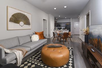 San Antonio apartment for rent - A living room with a grey couch, a round orange ottoman and a painting on the wall.
