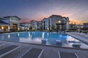 San Antonio apartment for rent - A large swimming pool surrounded by lounge chairs and buildings in the background.