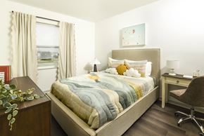 Columbus apartment for rent - Bright, modern bedroom with a large window, soft neutral curtains, and a stylish upholstered bed paired with a cozy workspace area.