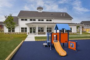 Selkirk apartment for rent - A playground with a yellow slide and orange and blue play structures in front of a white building with a black roof.