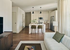 Las Vegas apartment for rent - A modern kitchen with white cabinets and a white couch with a green pillow.