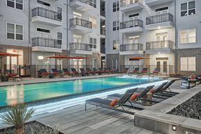 Houston apartment for rent - A swimming pool surrounded by lounge chairs and umbrellas in front of apartment buildings.