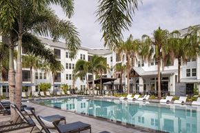 Kissimmee apartment for rent - A pool surrounded by palm trees and lounge chairs.