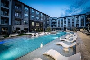 Houston apartment for rent - A large swimming pool with lounge chairs is surrounded by apartment buildings.