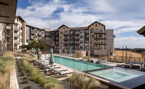 Austin apartment for rent - a large pool with chairs and umbrellas in front of an apartment building