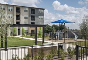 Fort Worth apartment for rent - A playground with a blue umbrella is in front of a building.