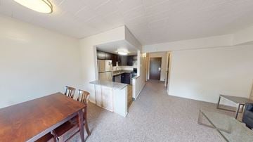 Ann Arbor apartment for rent - A room with a wooden table and chairs in the foreground and a kitchen area in the background.