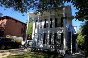 Ann Arbor apartment for rent - A white two-story house with black shutters and a black car parked in front.