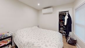 Ann Arbor apartment for rent - A bedroom with a bed, a window with blinds, a coat rack with clothes, and a bag on the floor.