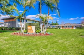 Escondido apartment for rent - a building with palm trees and a sign in the grass