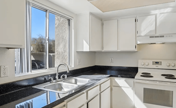 Cathedral City apartment for rent - A kitchen with white cabinets and a black countertop.