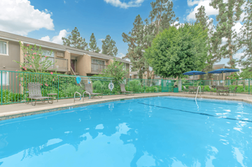 Orange apartment for rent - A swimming pool in front of a building with trees and bushes.