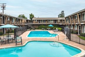 Orange apartment for rent - A swimming pool surrounded by a black fence and chairs.