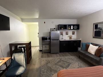 Omaha apartment for rent - A living room with a grey couch and a kitchen area with a fridge and dishwasher.