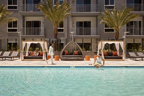 Woodland Hills apartment for rent - A woman is sitting on the edge of a pool in front of a building with palm trees.