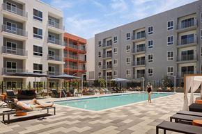 Woodland Hills apartment for rent - A woman is standing in the pool area of a hotel with a pool, sun loungers and umbrellas.