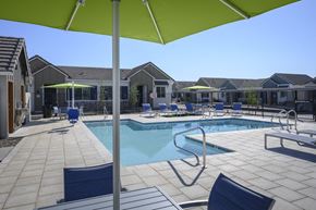 Chandler apartment for rent - a swimming pool with chairs and umbrellas in front of a house at Village of Chandler Apartments, Chandler, Arizona