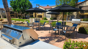 Sun City apartment for rent - A BBQ grill is in the foreground of a patio with chairs and umbrellas.