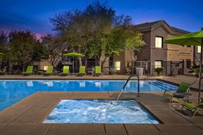 Tucson apartment for rent - A swimming pool surrounded by chairs and umbrellas at dusk.