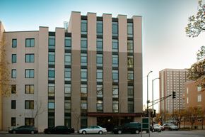 Chicago apartment for rent - A large building with a lot of windows is in the middle of a street with cars parked in front.