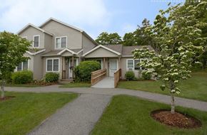 East Sandwich townhouse for rent - A house with a grey roof and a white door is surrounded by greenery.