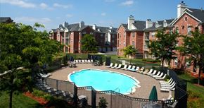 Omaha apartment for rent - an outdoor pool with lounge chairs and umbrellas in front of a brick building