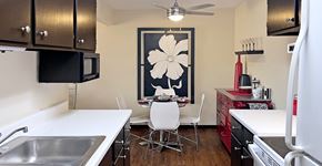 Omaha apartment for rent - Fully equipped kitchen with black cabinets, ample countertop space, wood laminate flooring, and dining area at Kensington Woods Apartments