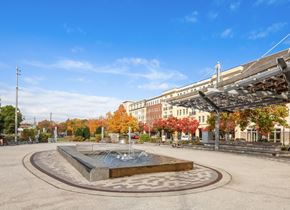 Wyandanch apartment for rent - A fountain in the middle of a plaza with buildings and trees in the background.
