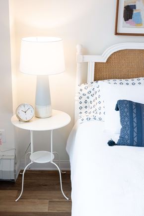 Wyandanch apartment for rent - A white bedside table with a lamp and clock beside a bed.