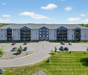 Fredericton apartment for rent - A large building with a parking lot in front of it.