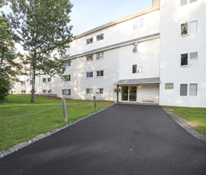Fredericton apartment for rent - A white building with a black driveway in front.